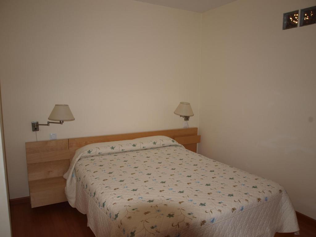 a bed in a bedroom with two lamps on the wall at Apartamentos Turísticos La Peña in Baños de Montemayor
