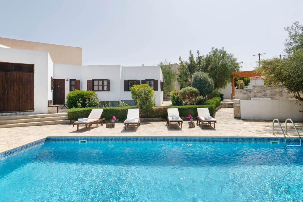 a swimming pool with chairs and a house at Meleni Cottage Houses in Parekklisha