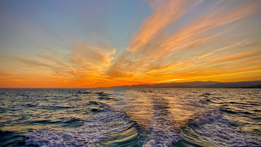 una puesta de sol en el océano con un barco en el agua en La terrazza sullo Jonio, en Roccella Ionica