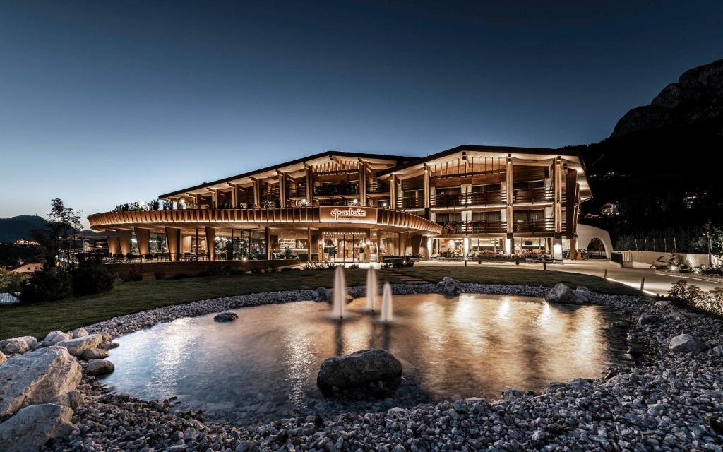 ein großes Gebäude mit einem Teich davor in der Unterkunft Granbaita Dolomites in Wolkenstein in Gröden