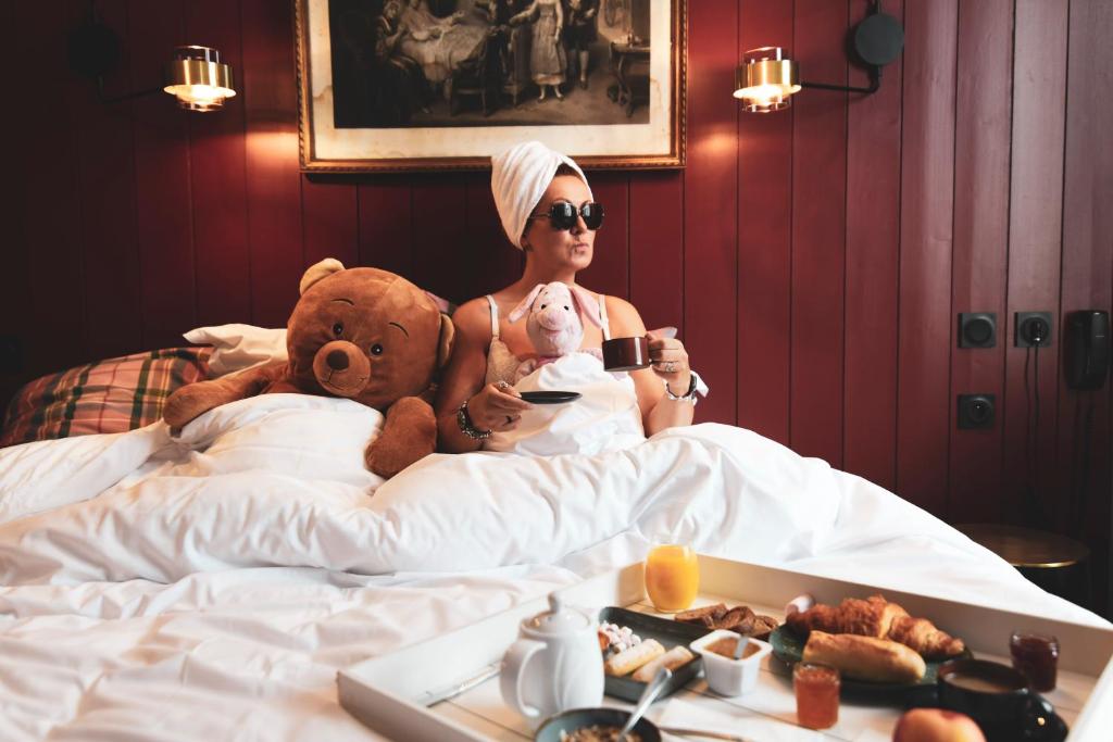 a woman sitting in bed with a teddy bear and a teddy bear at Naâd Hotel Sarlat Centre Ville in Sarlat-la-Canéda