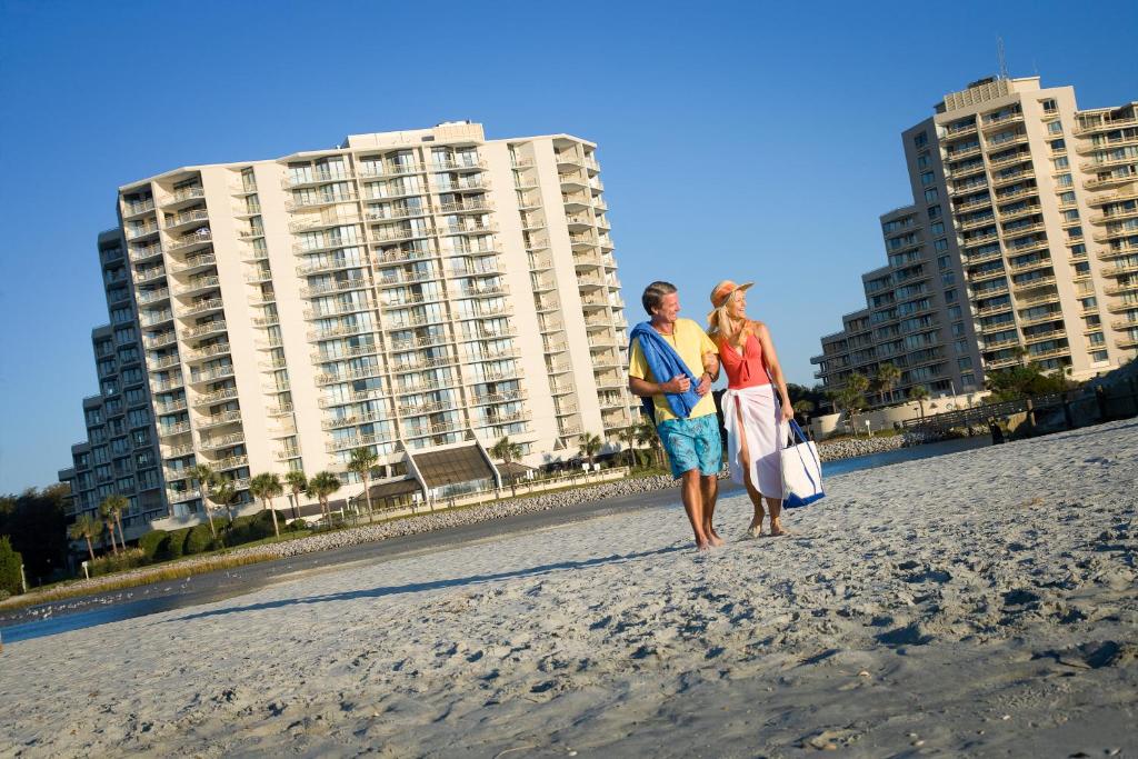 two women walking on the beach in front of buildings at Ocean Creek Resort in Myrtle Beach