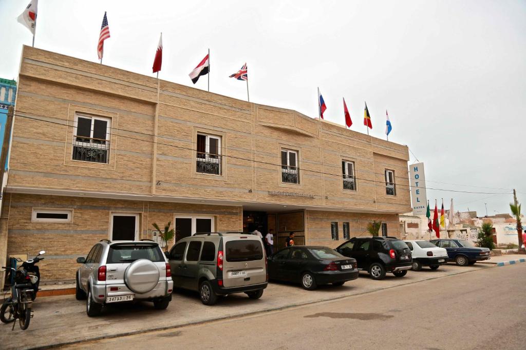 a building with cars parked in a parking lot with flags at Kasba TanTan in Tan-Tan Plage