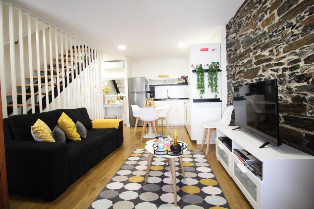 a living room with a black couch and a tv at Casa do Tablado - Foz Côa in Vila Nova de Foz Coa