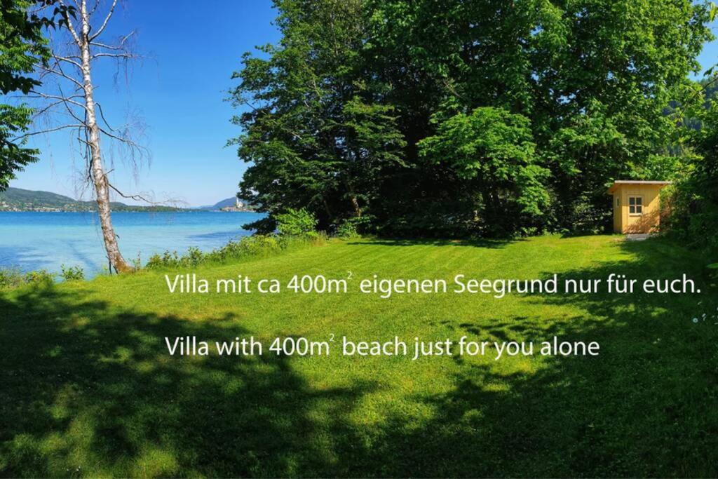 une photo d'un champ avec un lac et des arbres dans l'établissement Alte Villa 400m2 Seegrund nur für euch - old villa with 400m2 beach just for you, à Maria Wörth