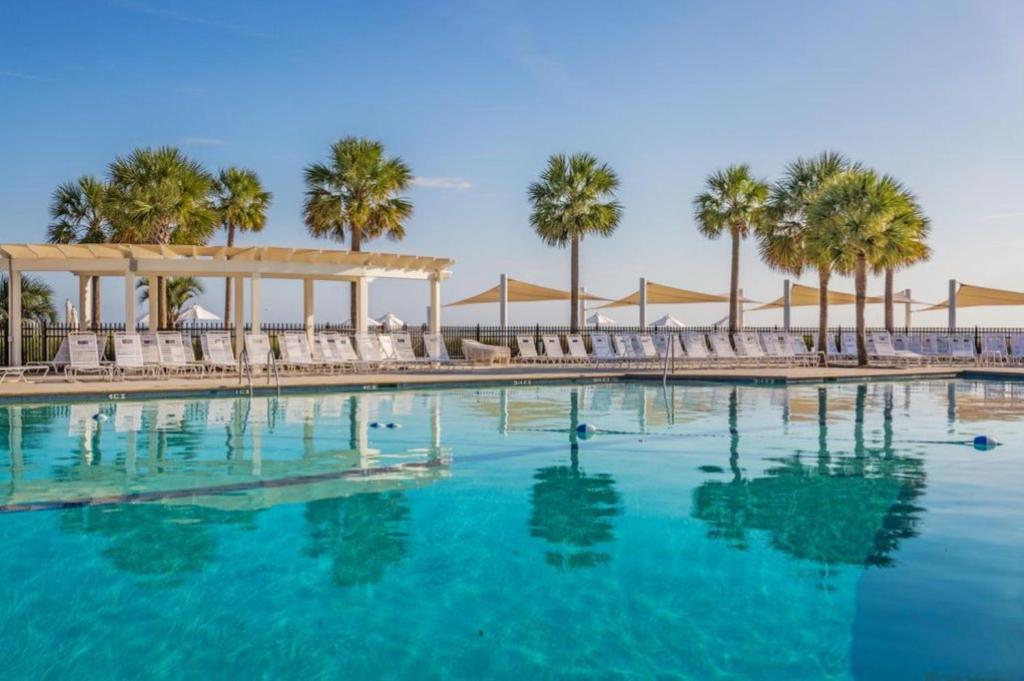 a swimming pool with chairs and palm trees at 1315 Pelican Watch - Seabrook Island - Beachfront 5 Star Condo - Fido Friendly in Seabrook Island