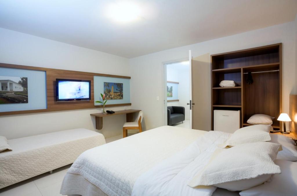 a white bedroom with a bed and a tv at Hotel Tavares Correia in Garanhuns