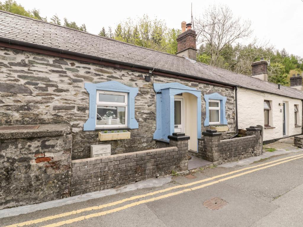 an old stone house with blue windows on a street at Crud yr Awel in Bangor