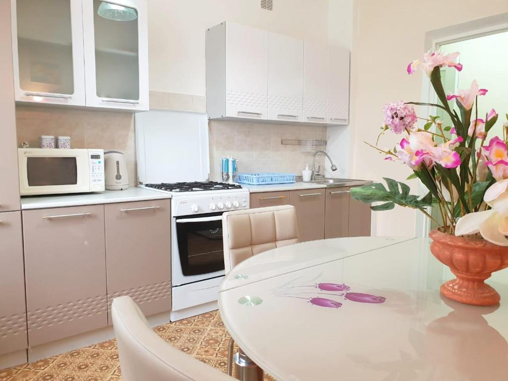 a white kitchen with a table and a vase of flowers at Шикарная Двухкомнатная in Atyraū