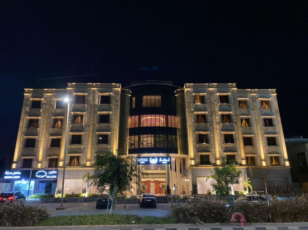 zwei Gebäude nachts mit vor ihnen geparkt in der Unterkunft Lotaz Hotel - Al Shatea in Dschidda