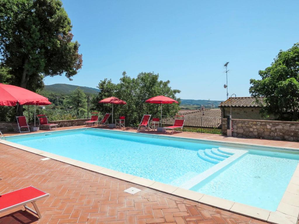 a swimming pool with chairs and red umbrellas at Apartment Giada by Interhome in Santa Luce