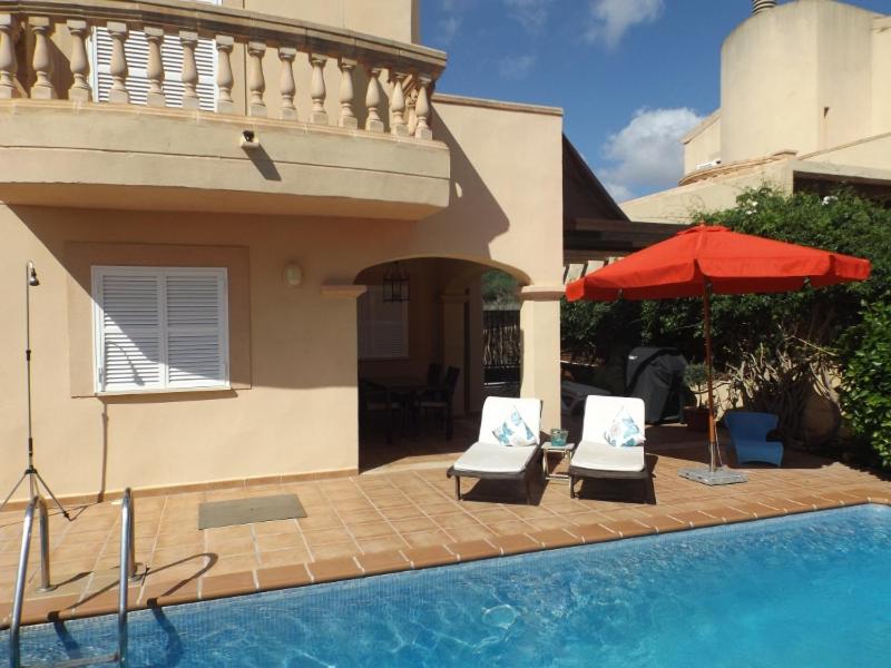 ein Haus mit zwei Stühlen und einem Sonnenschirm neben einem Pool in der Unterkunft Ferienhaus Casa Yelmo in Cala Mendia