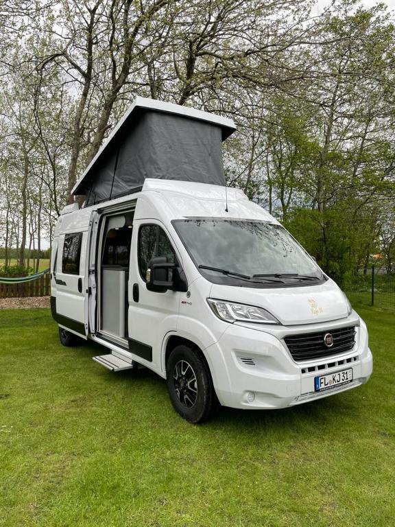 un camión blanco estacionado en un campo con una casa en el techo en Camper Van Koje 31, en Flensburg