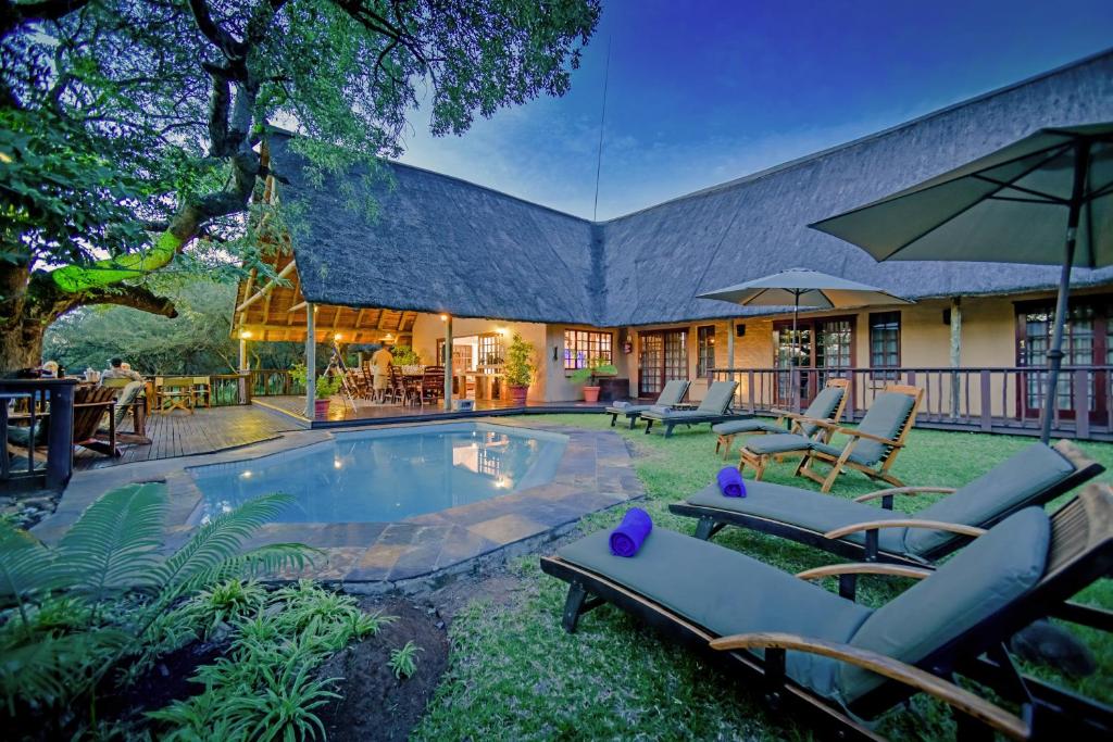 a house with a pool with chairs and an umbrella at Needles Lodge in Marloth Park