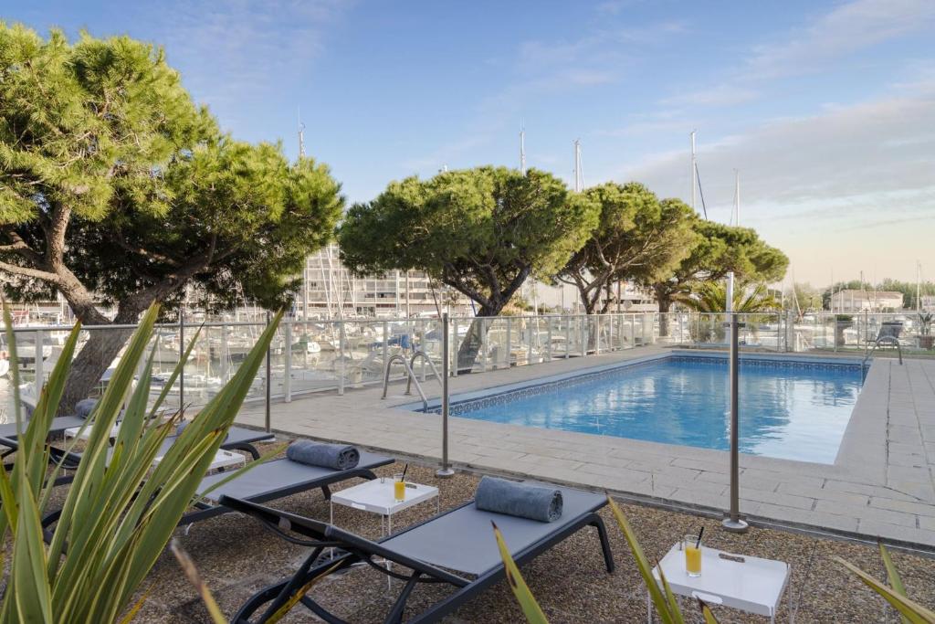 Elle offre une vue sur une piscine bordée de tables et d'arbres. dans l'établissement The Originals Boutique, Hôtel Neptune, Montpellier Sud (Inter-Hotel), à Carnon-Plage