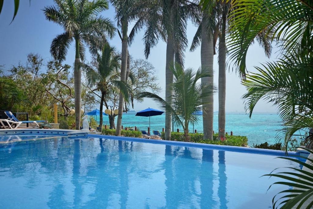 a swimming pool with palm trees and the ocean at Hotel La Joya Isla Mujeres in Isla Mujeres