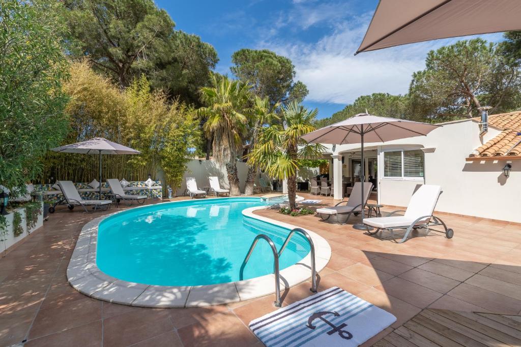 a pool with chairs and umbrellas next to a house at La Villa de l'Olivier in Cap d'Agde
