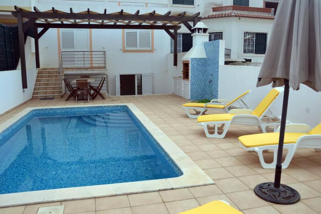 einen Pool mit Stühlen und einem Sonnenschirm auf einer Terrasse in der Unterkunft Moradia Fantástica com Piscina a 5 min da Praia in Monte Gordo