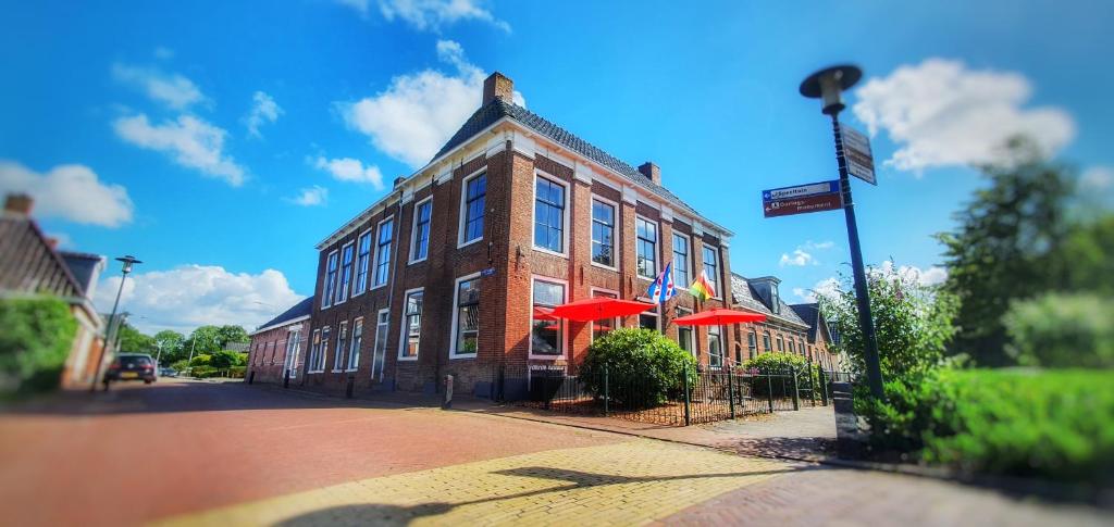 a large brick building with red umbrellas on a street at Herberg Het Rechthuis in Rinsumageest