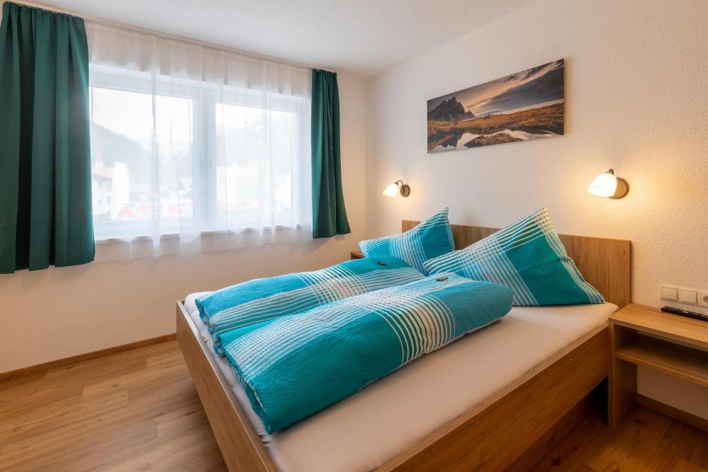- une chambre avec un lit doté de draps bleus et une fenêtre dans l'établissement Apart Elluto, à Sölden
