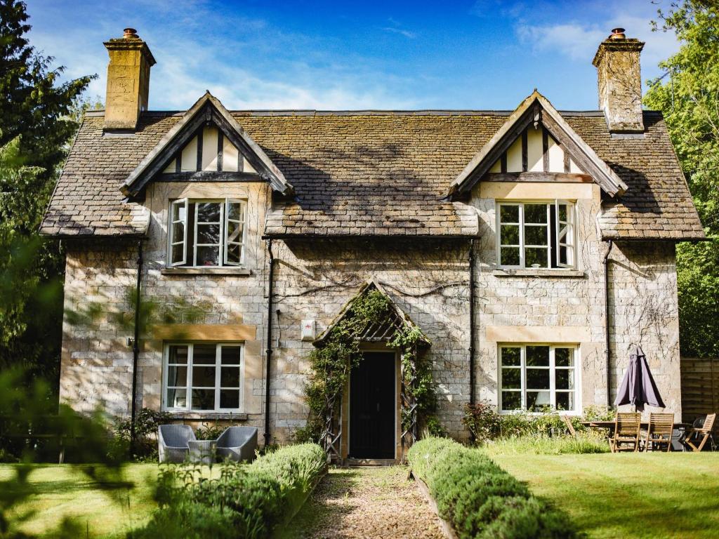 une ancienne maison en pierre avec des chaises en face de celle-ci dans l'établissement Sudeley Castle Guest Cottage, à Winchcombe