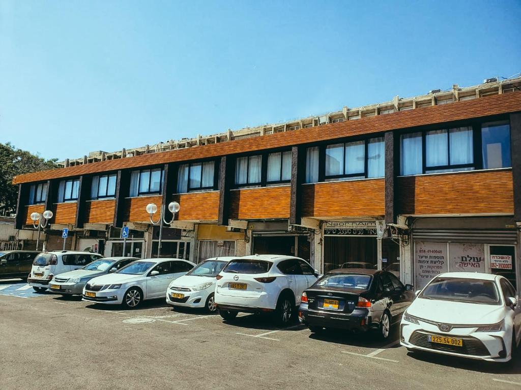 eine Reihe von Autos, die auf einem Parkplatz vor einem Gebäude geparkt sind in der Unterkunft Unique Hotel Ashdod in Aschdod