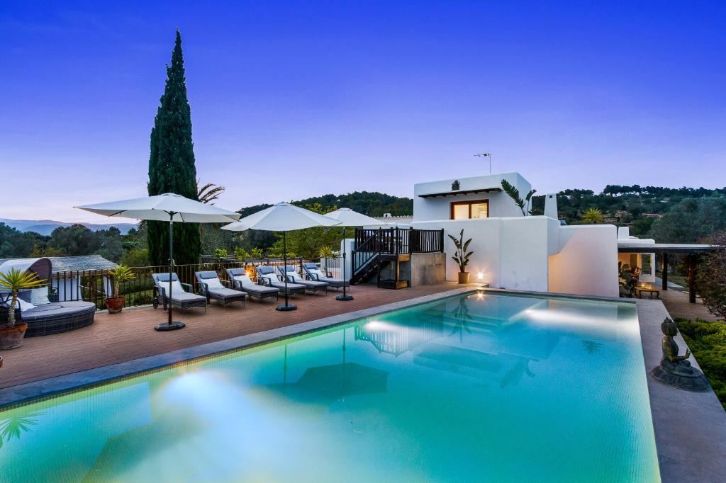 a swimming pool with chairs and umbrellas in front of a house at Can Skye in Sant Carles de Peralta