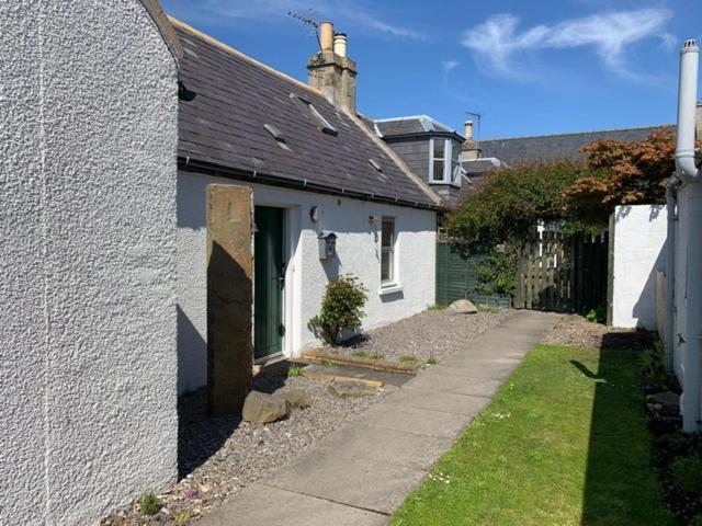 a small white house with a sidewalk next to a building at Abbey Cottage, Findhorn in Findhorn