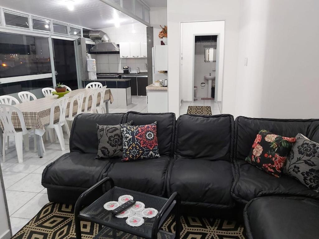 a living room with a black leather couch and a kitchen at Apto para até 6 pessoas, 600 metros da Basílica in Aparecida