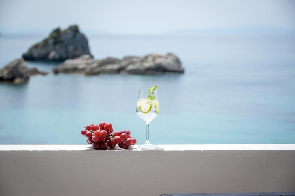 a glass of wine and grapes on a table in front of the ocean at Krioneri Beach in Parga