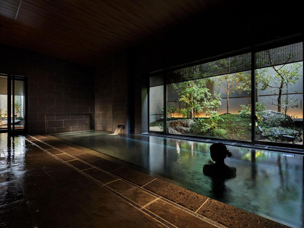 a swimming pool in a building with a person in the water at Onsen Ryokan Yuen Bettei Tokyo Daita in Tokyo