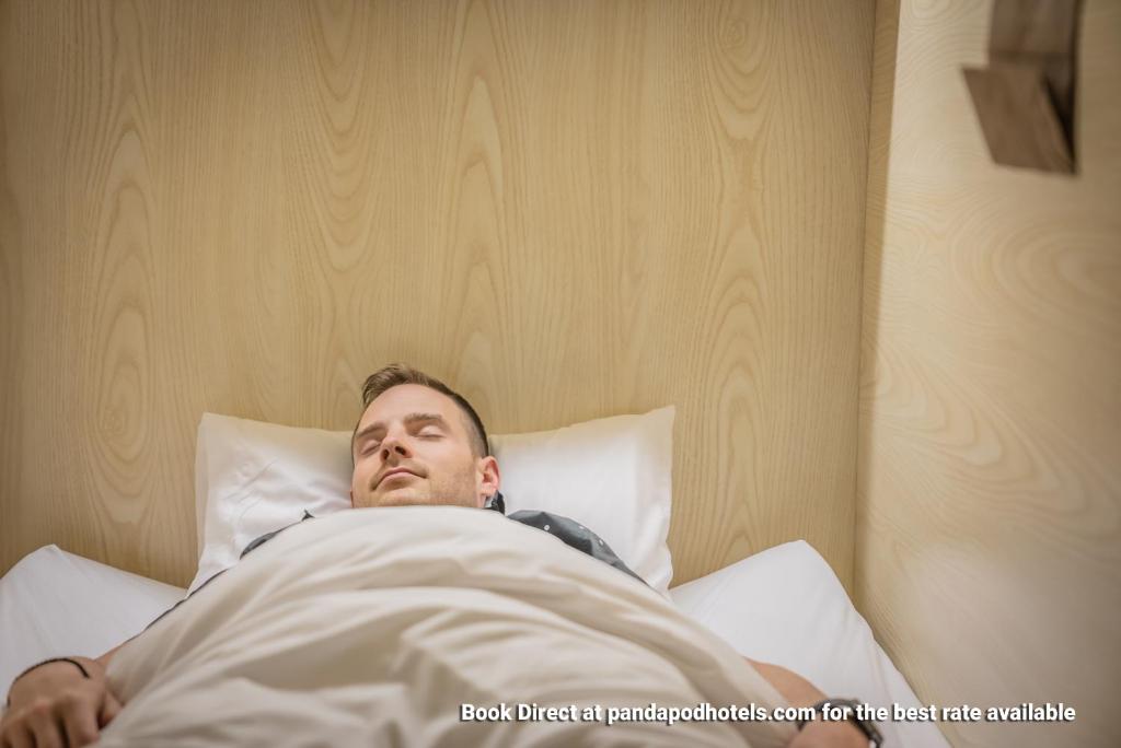 a man laying in bed under a blanket at Panda Pod Hotel in Richmond
