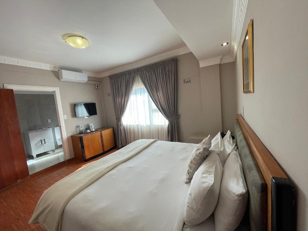 1 dormitorio con 1 cama grande con sábanas y almohadas blancas en Ngwenya Hotel & Conference Centre, en Klerksdorp