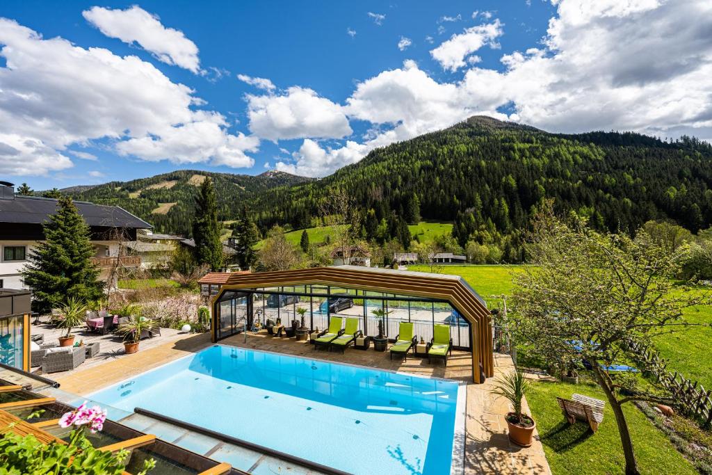 an outdoor pool with a pavilion and mountains in the background at Genusshotel Almrausch in Bad Kleinkirchheim