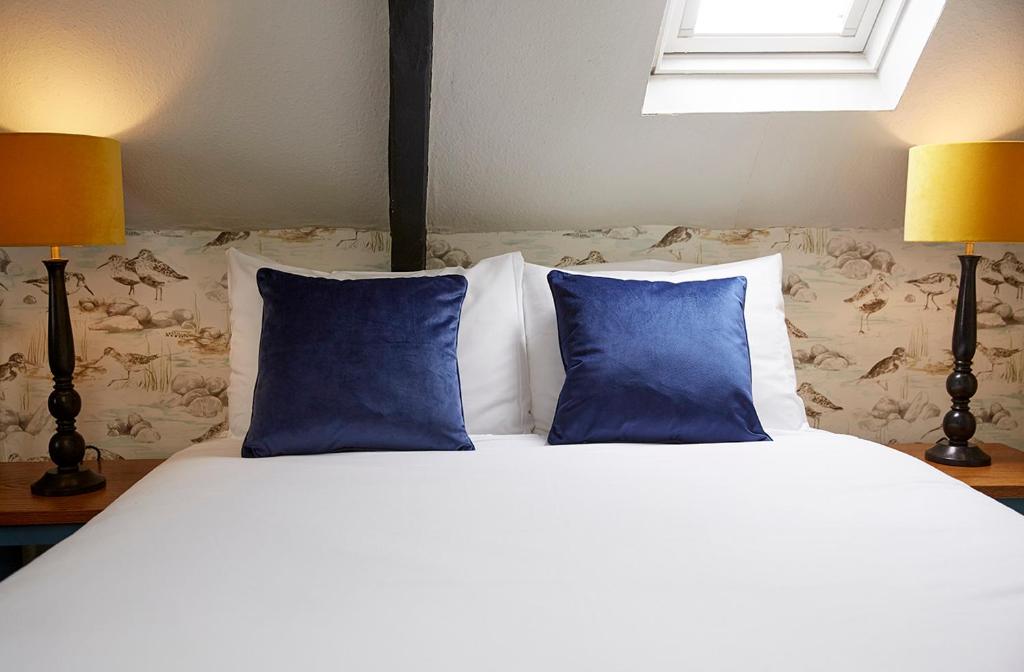 a bed with two blue pillows and two lamps at Old Manse Hotel by Greene King Inns in Bourton on the Water