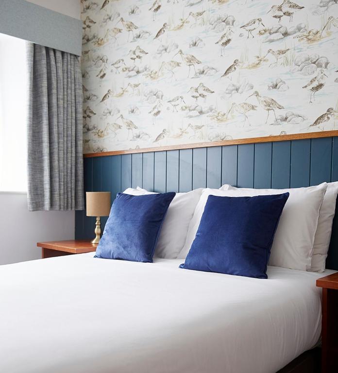 a large white bed with blue pillows in a bedroom at Old Manse Hotel by Greene King Inns in Bourton on the Water