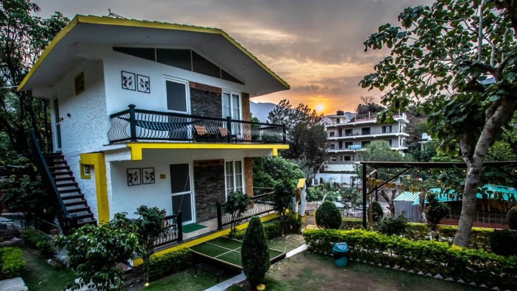 a white house with a balcony and a tree at The Hosteller Rishikesh, Tapovan in Rishīkesh