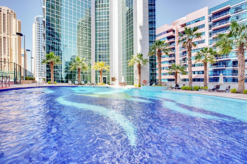 a large swimming pool with palm trees and buildings at The Waves by DAMAC, Dubai Marina in Dubai