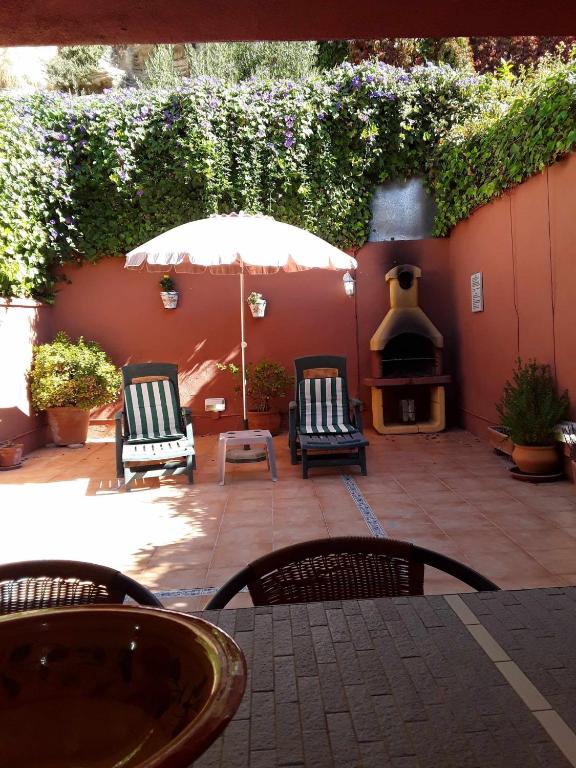 a patio with two chairs and an umbrella and a fireplace at Viviendas Turísticas Los Arrayanes in Ronda