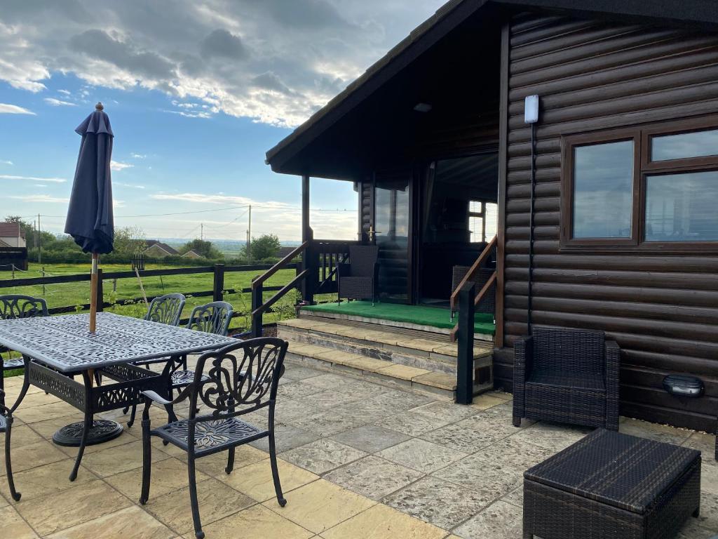 a patio with a table and chairs and an umbrella at Rew Farm Country & Equestrian Accommodation - Sunrise Lodge in Melksham