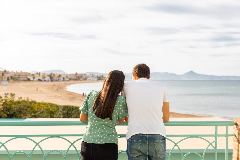 a man and woman standing on a balcony looking at the beach at Hotel Noguera Mar in Denia