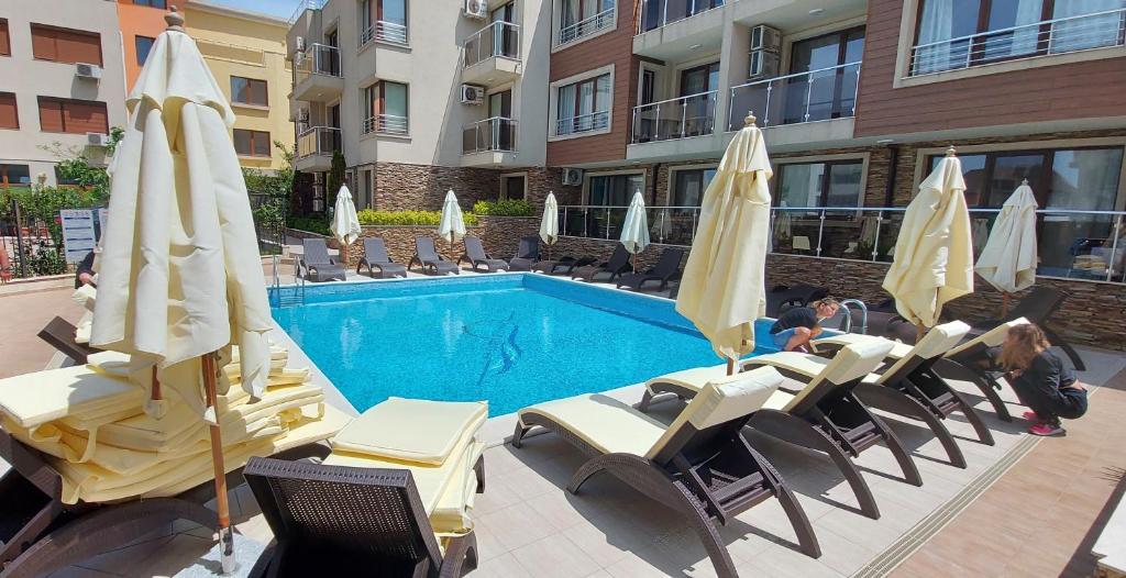 a pool with chairs and umbrellas in front of a building at Менада Хоризонт Апартаменти in Sozopol
