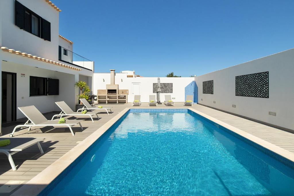 a swimming pool with chairs and a house at Villa Tropicana in Albufeira