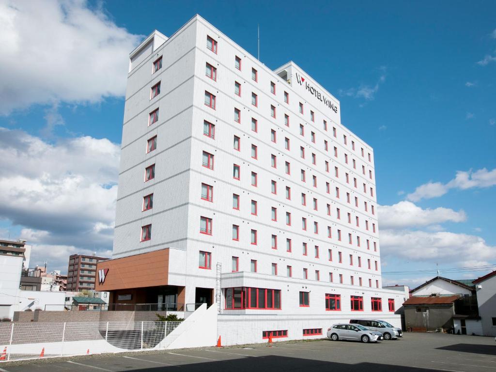 a white building with a car parked in front of it at Hotel Wing International Chitose in Chitose