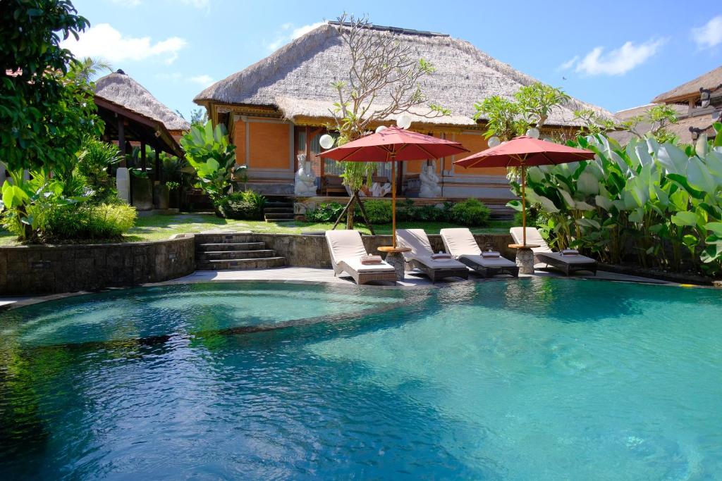 a pool with chairs and umbrellas in front of a house at Puri Andong Villa in Ubud