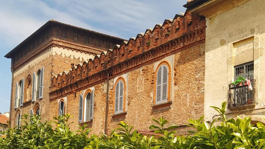 an old brick building with a balcony and trees at Scalo al Castello in Locate di Triulzi