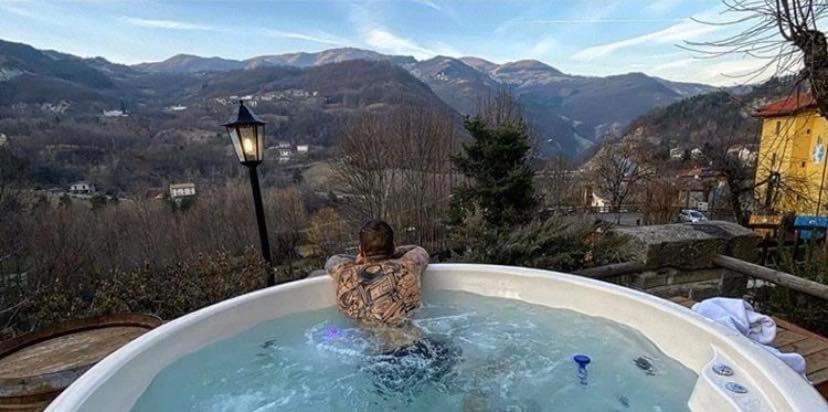 a man in a jacuzzi tub with a view of mountains at Casa Benassi Rooms, Apartament & Suite con Piscina panoramica e Wellness in Riolunato