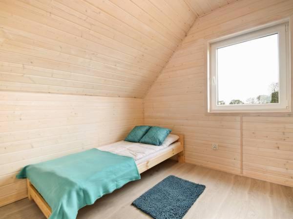 a small bed in a wooden room with a window at Domki Turkusowe Zacisze in Sarbinowo