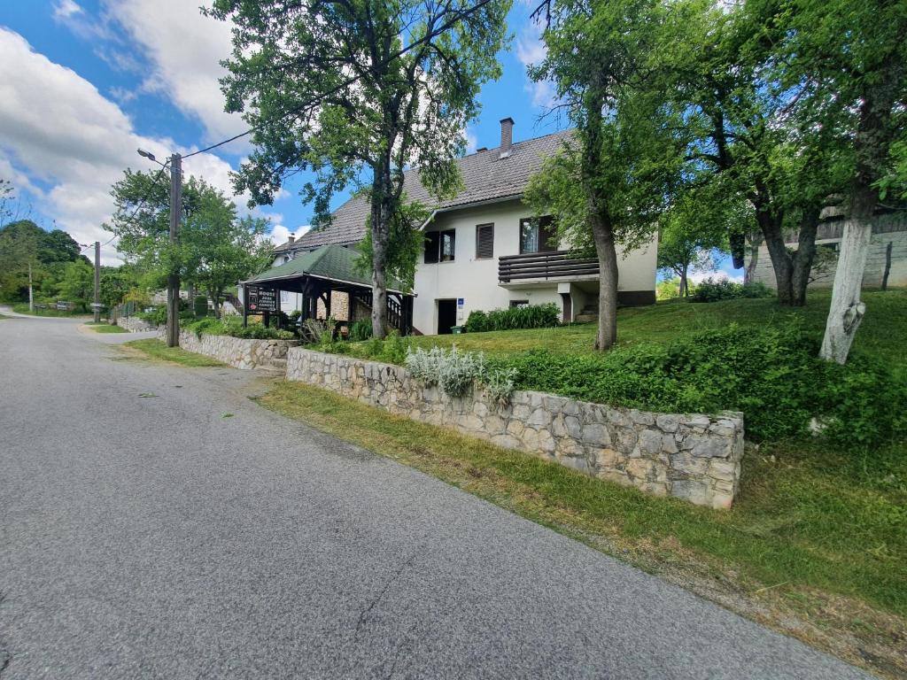 a white house with a stone retaining wall next to a street at Guest House Štefanija in Poljanak