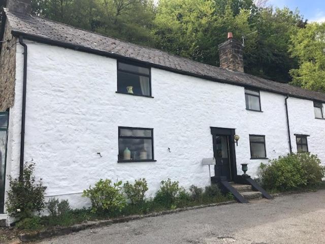 uma casa branca com uma porta preta e janelas em Historic 17th century farmhouse in Wales em Gwernymynydd